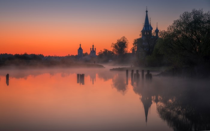 Sunrise over river with churches and fog in Dunilovo