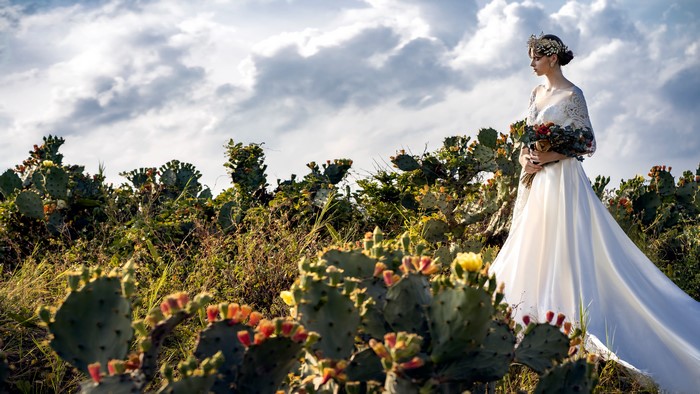 Bride in a wedding dress holding a bouquet in a cactus field