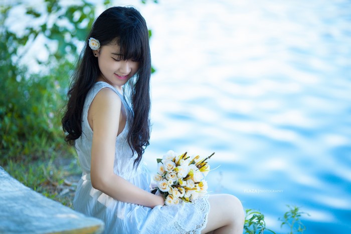 Brunette girl with bouquet sitting by water