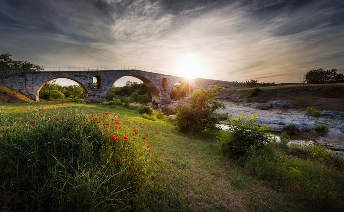 Stone bridge over a stream at sunset with poppies