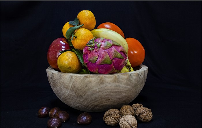 Fruit bowl with oranges, dragon fruit, banana, apple, tomatoes, walnuts, and chestnuts