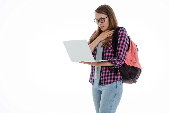 Female student with glasses and backpack looking at laptop with surprise