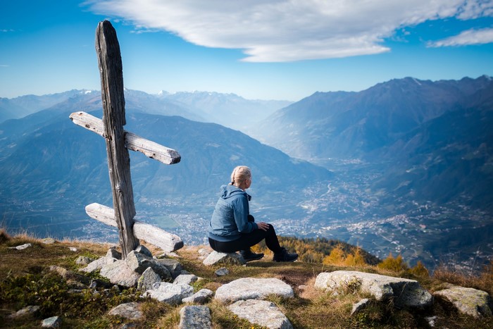 Woman sitting by wooden cross overlooking valley