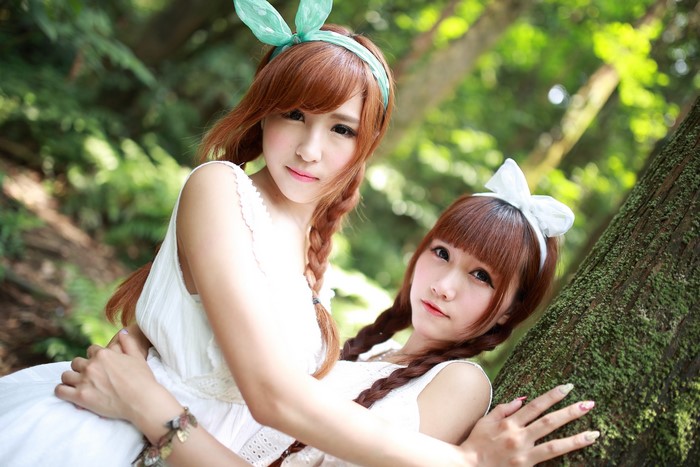 Two Asian girls with braided hair and bows in a forest