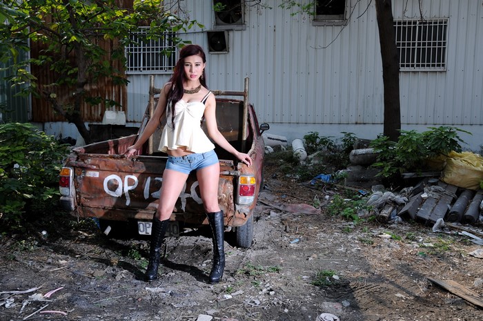 Asian woman in shorts and boots posing by a rusty truck