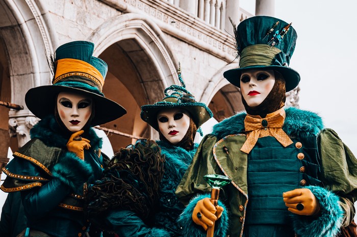 Three people in Venetian carnival costumes and masks