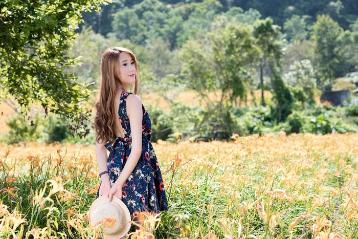 Asian woman in floral dress holding hat in flower field