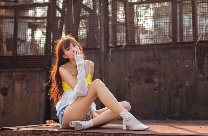 Asian woman in yellow singlet and denim shorts sitting