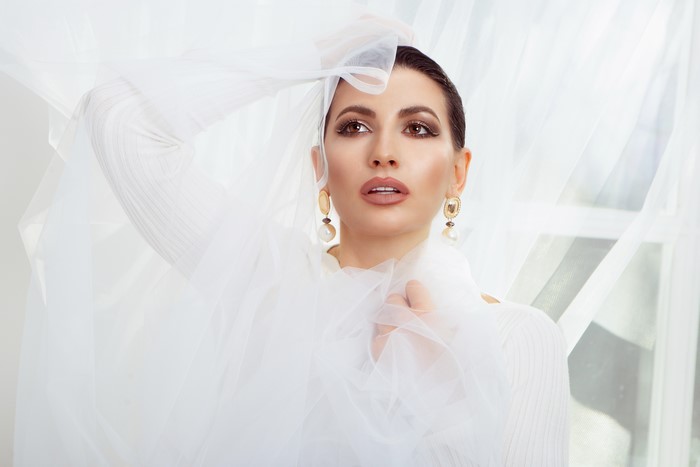 Brunette woman with earrings and makeup behind sheer fabric
