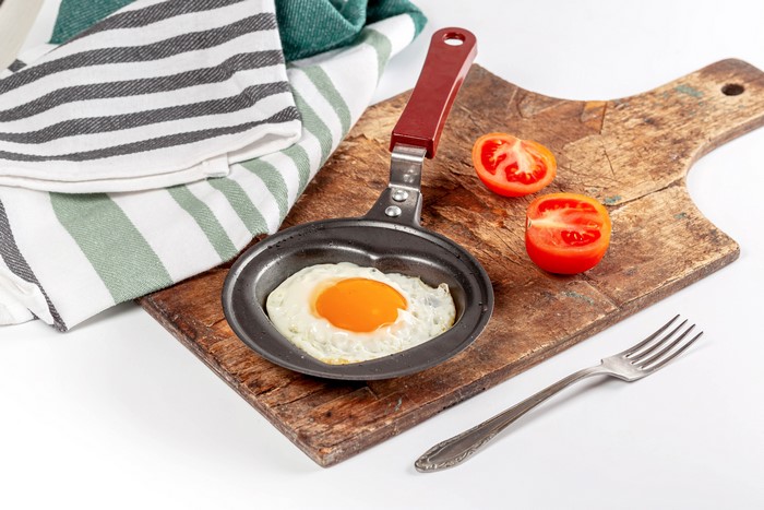 Fried egg in heart-shaped pan with tomatoes and fork