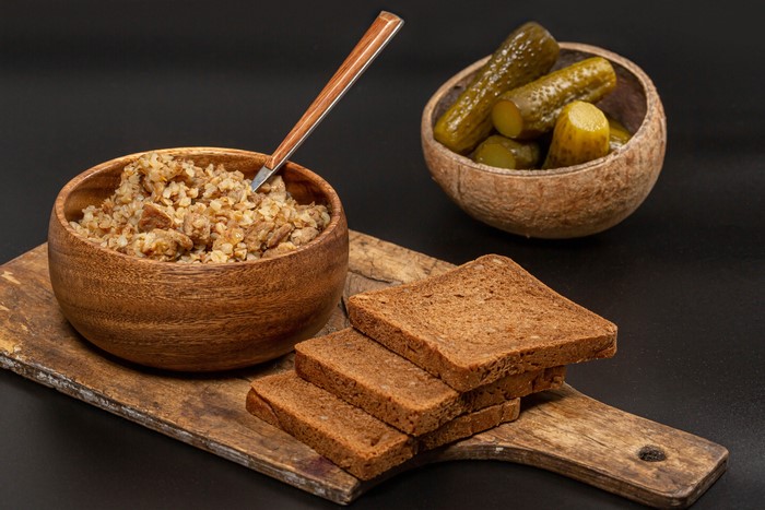 Buckwheat porridge with meat, pickles, and rye bread on a cutting board