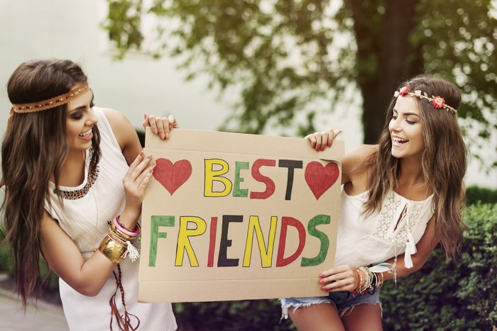 Two smiling young women holding a "BEST FRIENDS" sign