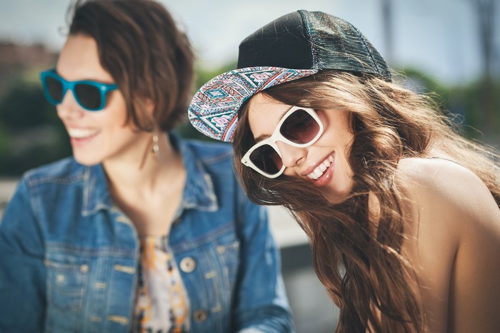 Two smiling women wearing sunglasses and baseball cap