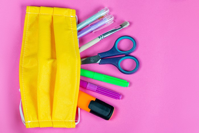 Yellow face mask with school supplies on pink background