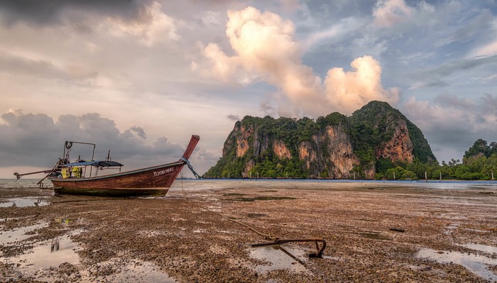 Longtail boat on a muddy shore with limestone cliffs in Krabi, Thailand