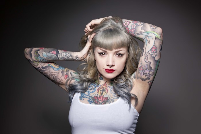 Woman with tattoos and piercings on gray background