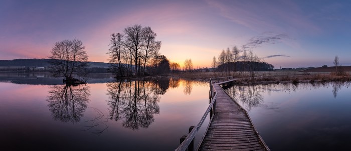 Wooden bridge over lake at sunrise with trees and reflections