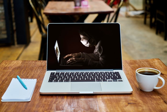 Laptop with person wearing mask, coffee, and notepad