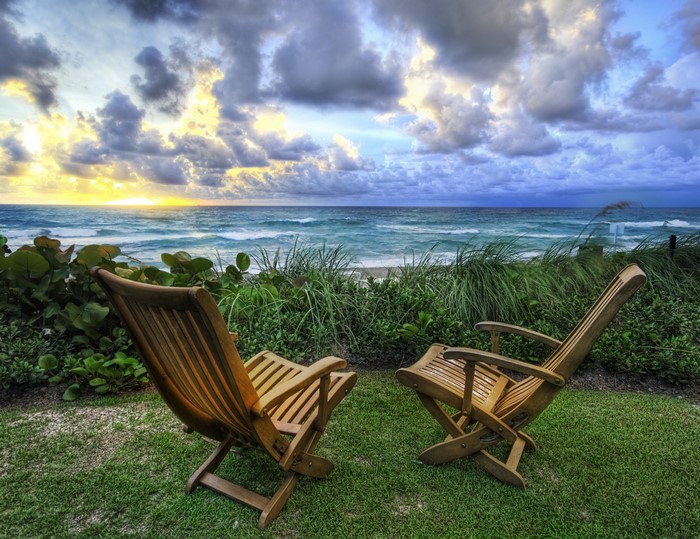 Two wooden chairs on grass overlooking the ocean at sunrise