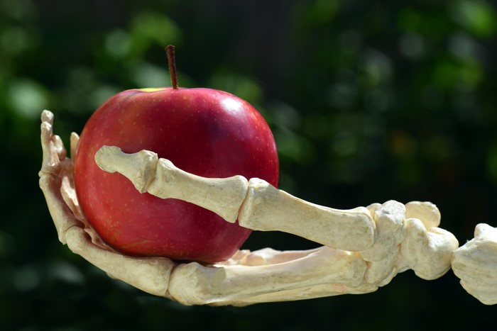 Skeleton hand holding a red apple