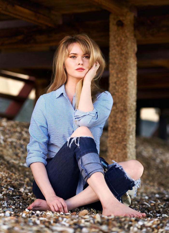 Blonde woman sitting on a beach in ripped jeans