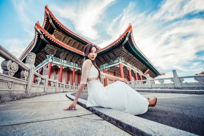 Asian woman in white dress sitting near traditional building