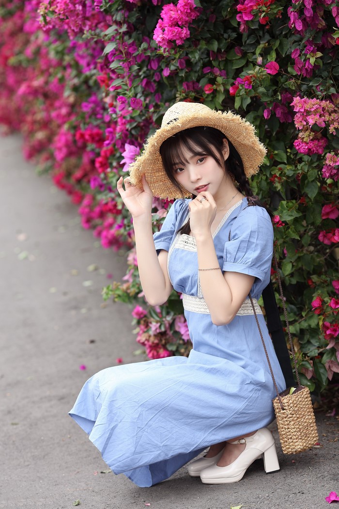 Asian woman in blue dress and straw hat posing by flowers