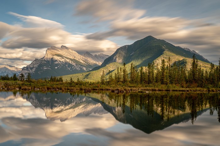 Mountains reflected in a calm lake with trees and clouds