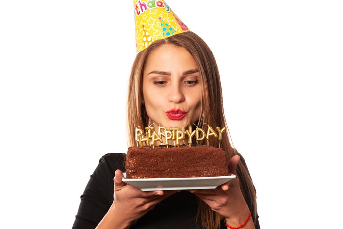 Woman in Birthday Hat Blowing Out Candles on Cake