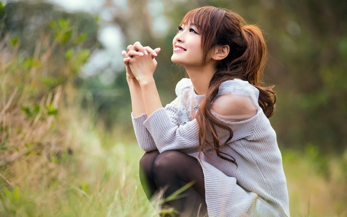 Asian woman with brown hair praying outdoors