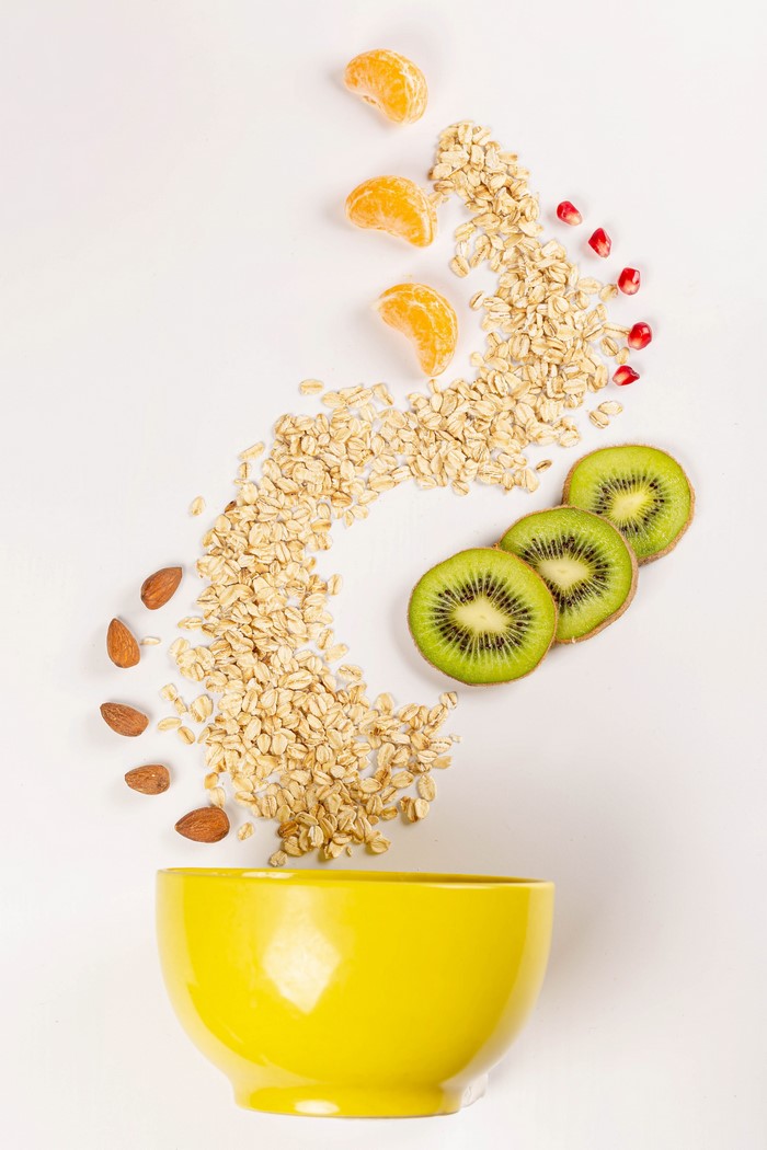 Oatmeal with kiwi, tangerine, almonds, and pomegranate seeds in a yellow bowl