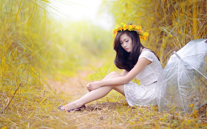 Brunette girl with flower wreath sitting by umbrella