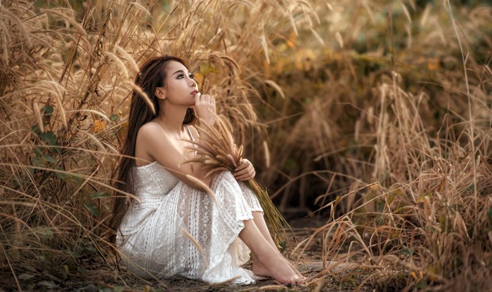 Asian woman in white dress sitting in tall grass