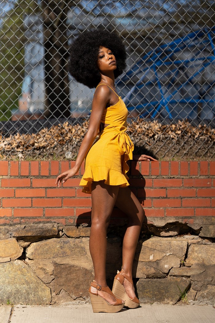 Woman in yellow dress posing by brick wall