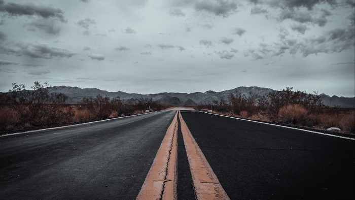 Desert road with mountains under overcast sky