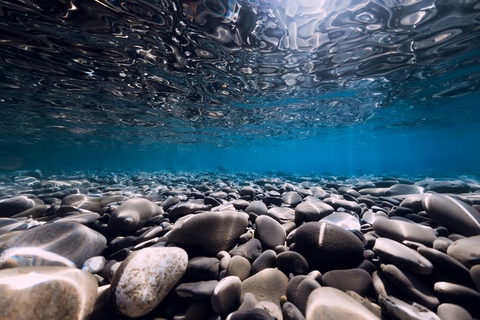 Underwater view of a rocky seabed with sunlight filtering through the water
