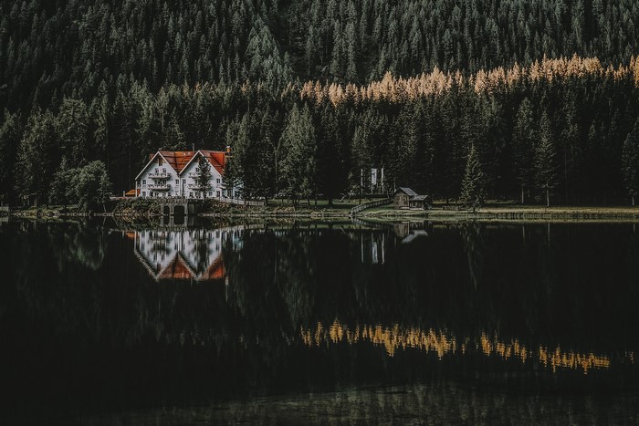 White house with red roof reflected in a dark lake surrounded by a forest