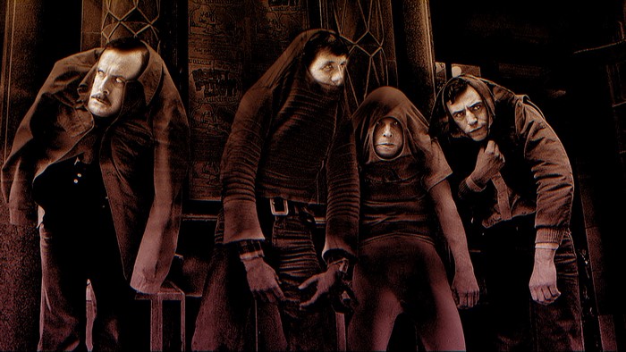 Four men in dark clothing with hoods