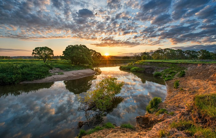 Sunrise over a river with trees and clouds