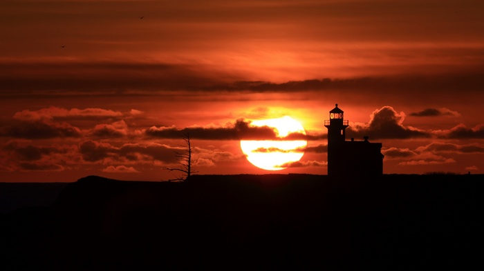 Silhouette of a lighthouse against a fiery sunset