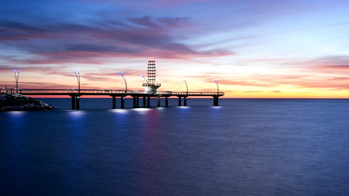 Pier with tower and lights over water at sunset