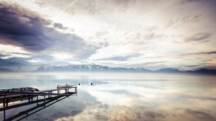 Wooden pier on a calm lake with snow-capped mountains in the distance