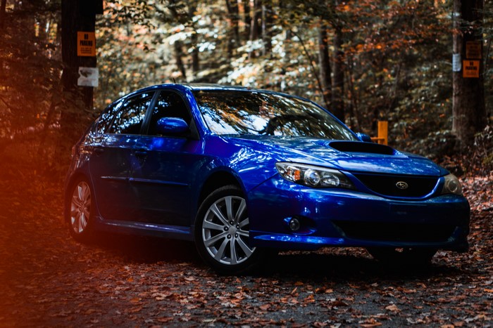 Blue Subaru Impreza WRX parked on a leaf-covered path in a forest