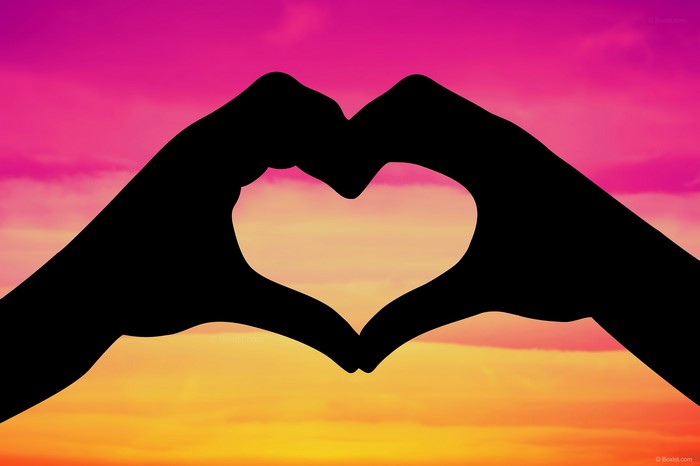 Silhouette of hands forming a heart against a sunset sky