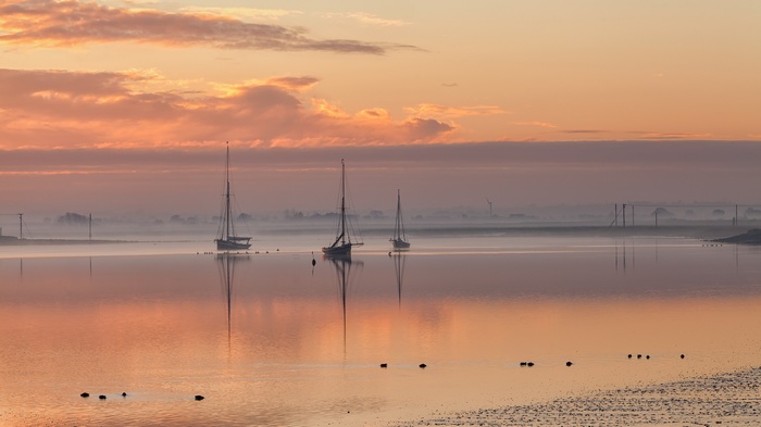Sailboats on misty water at sunrise