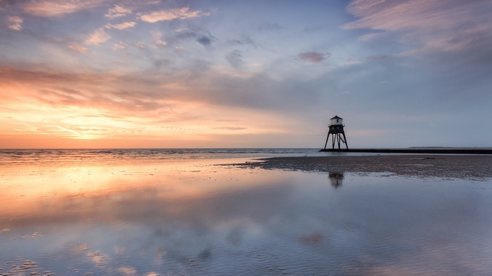 Lighthouse on stilts reflected in water at sunset