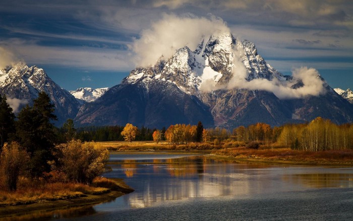 Snowy mountains reflected in a river with autumn trees