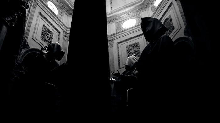 Monks in cloaks in a dimly lit ornate building