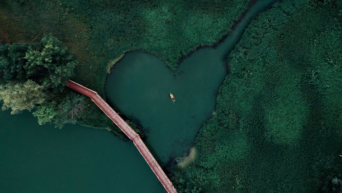 Aerial view of a heart-shaped lake with a boat and bridge