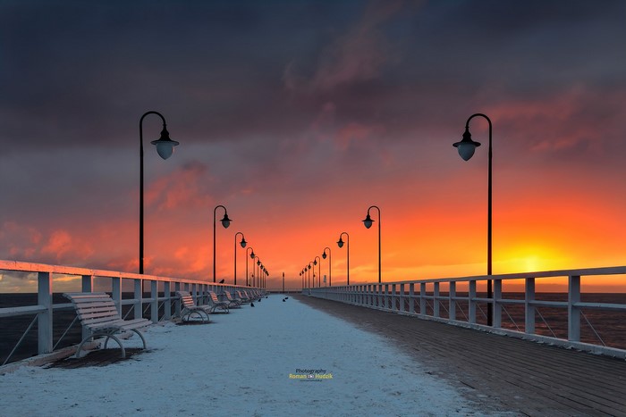 Snow-covered pier with streetlights at sunset